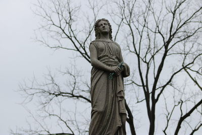 Low angle view of statue against bare trees during winter