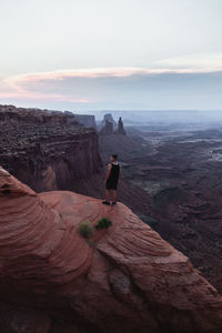 Rear view of man standing on rock against sky