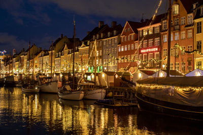 Sailboats moored on illuminated canal by buildings in city at night