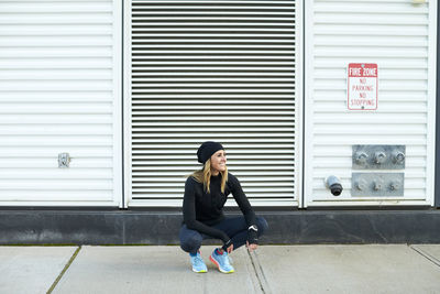 Full length of woman sitting against closed shutter