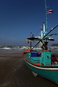 Boat moored on beach against clear blue sky