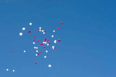 Low angle view of balloons flying against blue sky