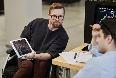 Disabled businessman showing cryptocurrency graph on tablet pc to colleague in office