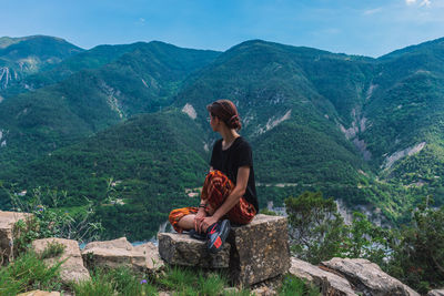 Man sitting on mountain looking at mountains against sky