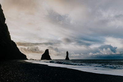 Silhouette beach by sea against sky