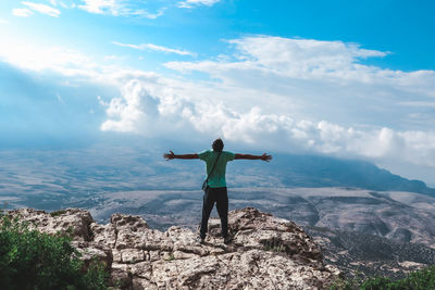 Rear view of man standing on rock against sky