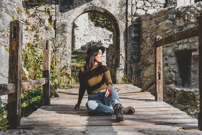 Young woman sitting on footbridge of old castle ruin, autumn, fall, earth tones, style.