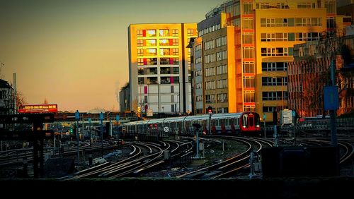 Train on railroad tracks by buildings against sky during sunset