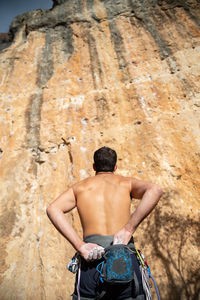 Rear view of shirtless man standing against rock formation