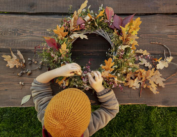 Boy wearing knit hat making autumn wreath on wooden table
