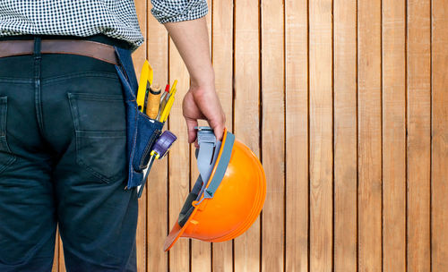 Midsection of engineer with work tools standing against wooden wall