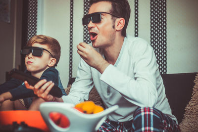 Father and son eating popcorn while watching movie at home