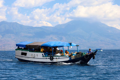 People on boat in sea against mountains