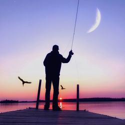 Silhouette man fishing in sea against sky during sunset