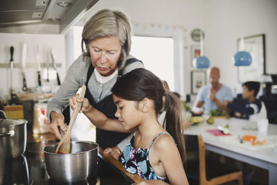 Grandmother looking at girl cooking at kitchen counter