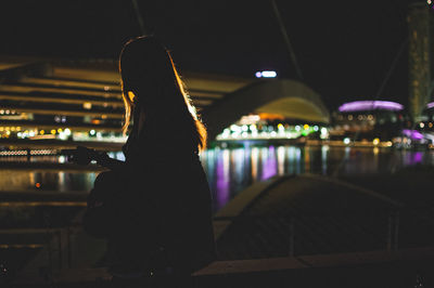 Side view of woman standing by illuminated bridge against sky at night