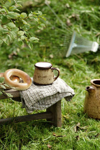 Cup with milk, pastries and jug wooden stool with checkered napkin, grass and metal pitchfork 