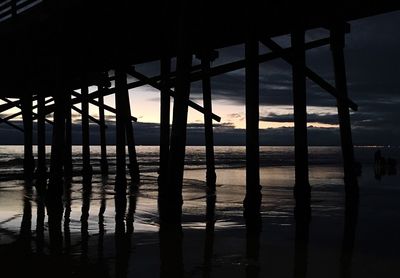 Silhouette bridge over sea against sky during sunset