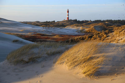 Lighthouse on beach by sea against sky