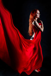 Side view of sensuous shirtless female model holding red fabric against black background