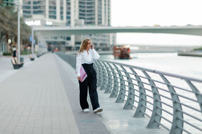 A blonde businesswoman holds a folder and talks on her smartphone in the city