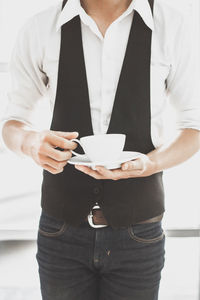 Midsection of man holding coffee cup against door