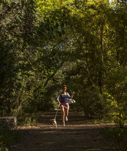 Woman with dog running amidst trees at forest