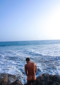 Rear view of naked man on rocks against sea