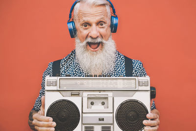 Portrait of male hipster holding speaker against orange background