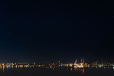 Illuminated city by sea against starry sky at night