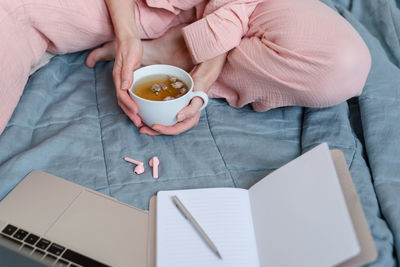 A scene in pastel colors of a woman making notes and drinking hot tea in her bed.