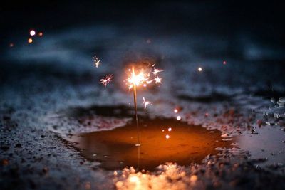 Close-up of lit sparkler in puddle at night