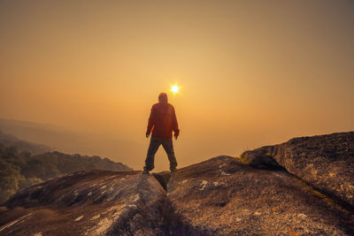 Man standing on cliff against sky during sunset