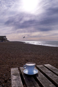 Close-up of coffee on table by sea against sky