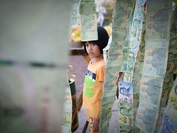 Side view of cute girl looking at paper currency hanging while standing outdoors