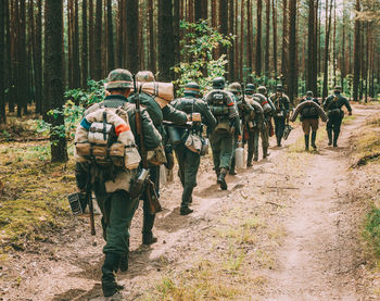 Rear view of army soldiers with equipment walking in row at forest