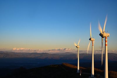 Wind turbines on landscape against sky during sunset