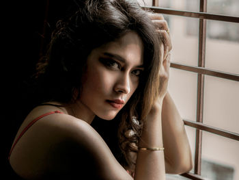 Close-up portrait of beautiful woman against window