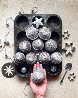 Directly above shot of hand holding cupcake over baking tray on stone table