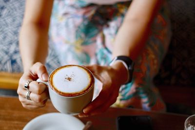 Midsection of woman holding coffee cup on table