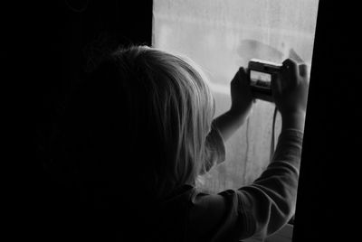 Rear view of boy photographing through window