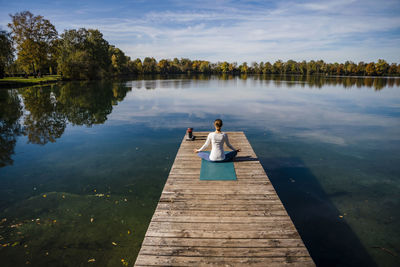 Woman meditating in front of lake under sky