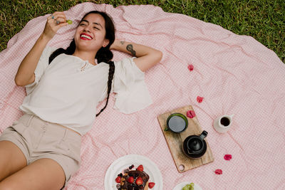 High angle view of woman having fruit while lying on picnic blanket in yard