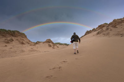 Rear view of man walking on sand at desert