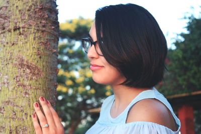 Side view of young woman touching tree trunk