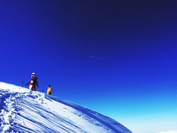 Low angle view of people on snowcapped mountain against clear blue sky