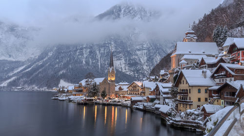 Buildings by trees against snow covered mountains during winter