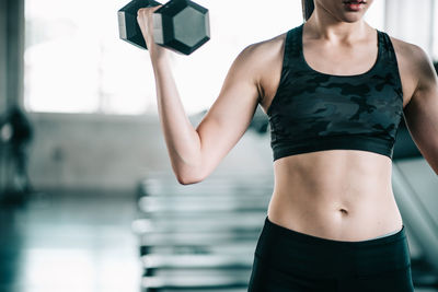 Midsection of woman lifting dumbbell in gym