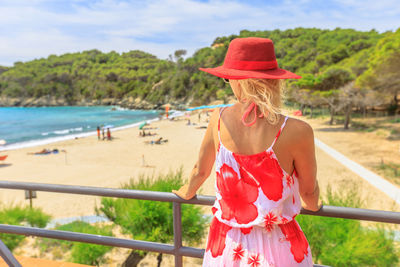 Rear view of woman standing by railing against sea