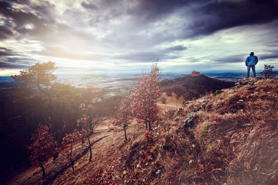 Rear view of man looking at view while standing on mountain against cloudy sky